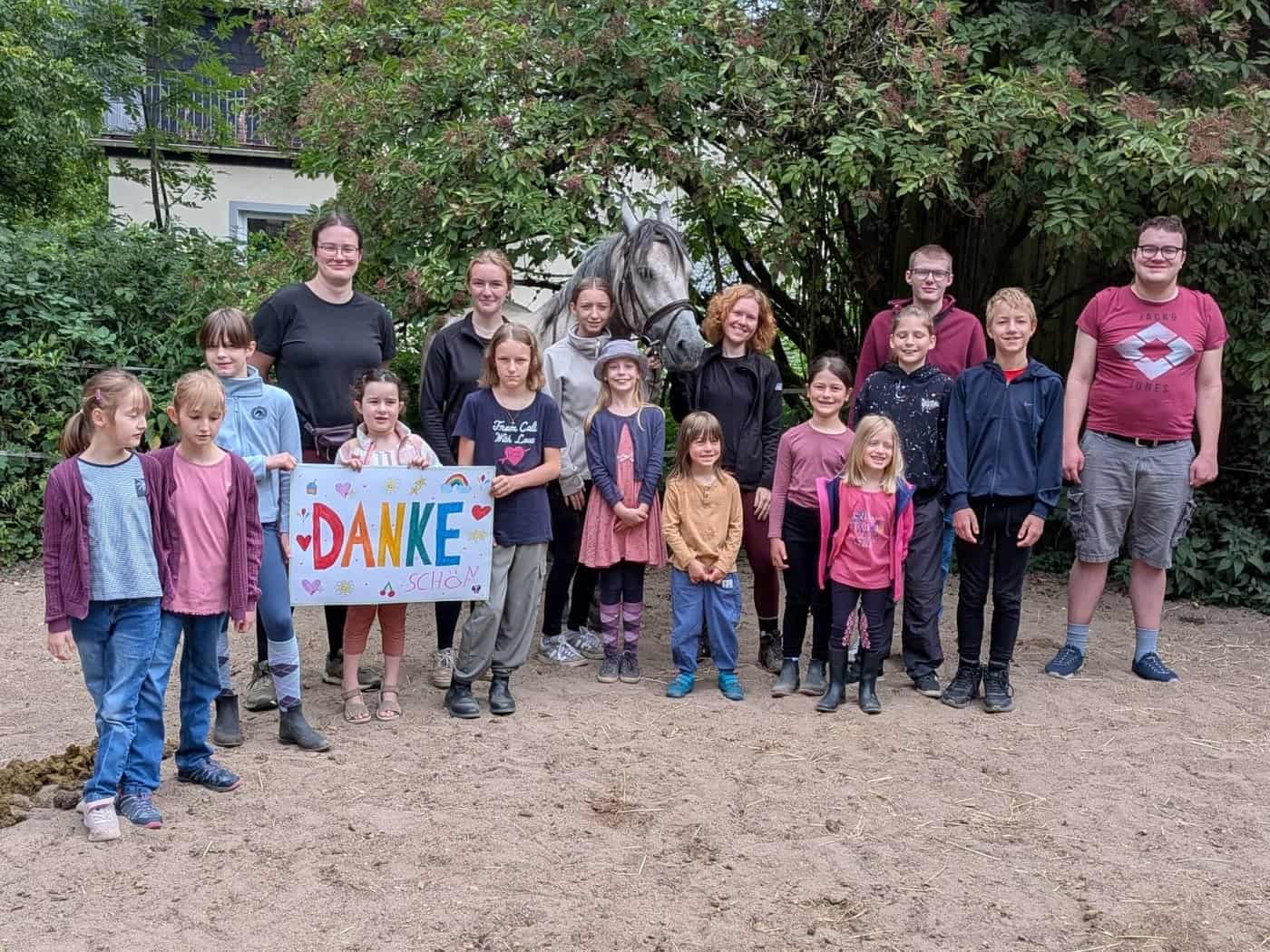 Kinder, Jugendliche und Betreuerinnen mit einem selbst gemalten Danke-schön-Schild neben dem neuen Therapiepferd